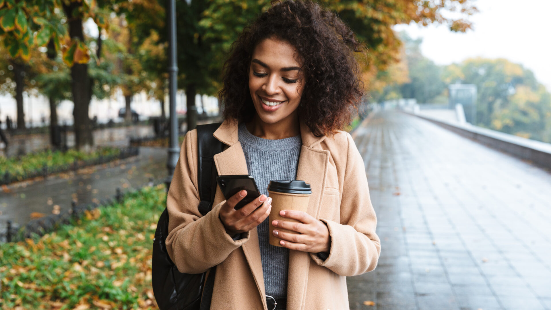 Woman walking and scrolling on phone with coffee.
