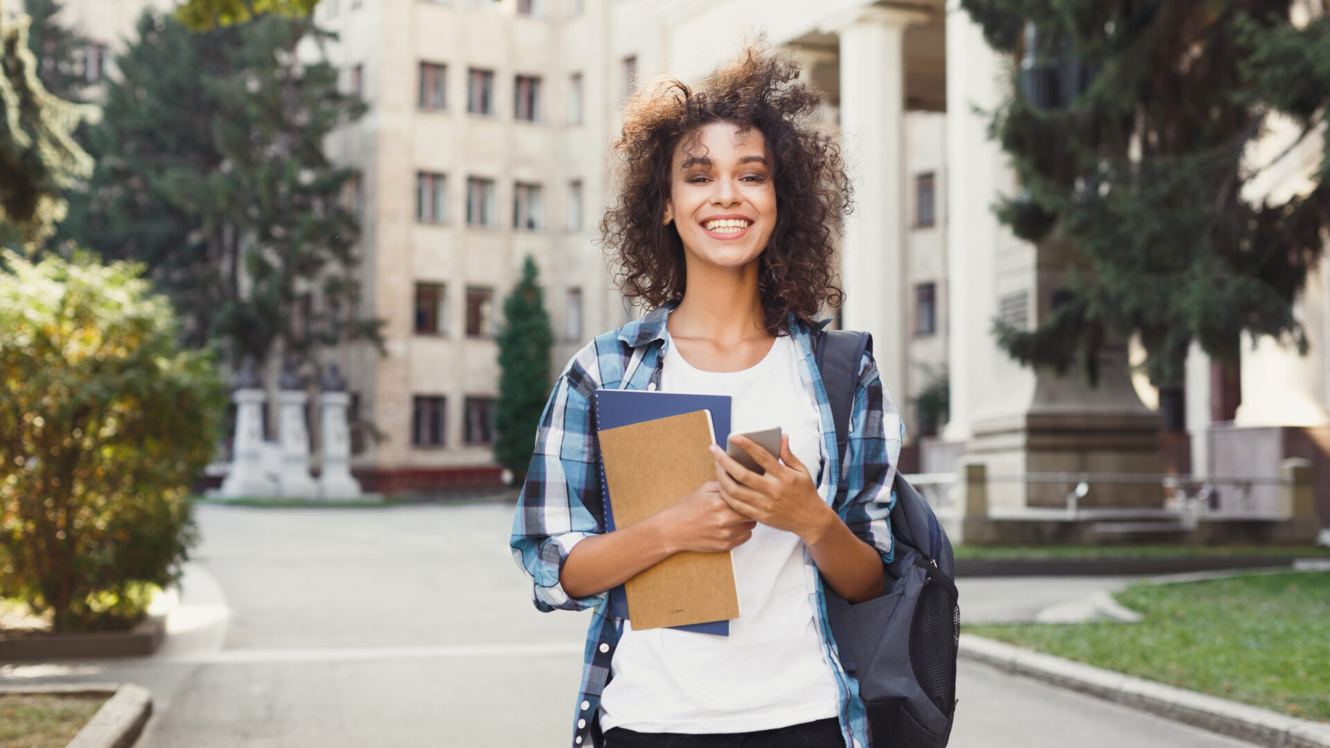 Happy college student holding books, supplies, and a backpack.